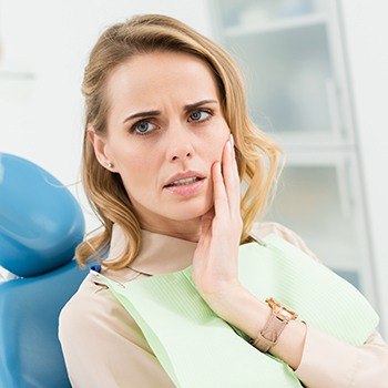 Woman holding cheek at emergency dentistry appointment