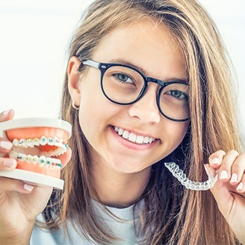 Teen holding Invisalign tray and model smile with braces
