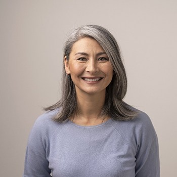 Older woman in grey shirt smiling with grey background