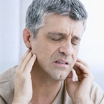 Man in need of TMJ therapy holding jaw joints