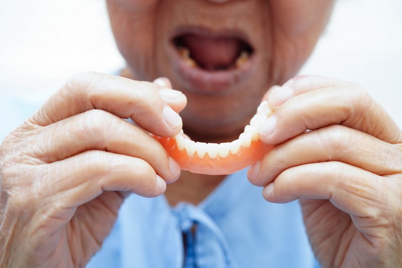 A closeup of an older woman holding an ill-fitting denture in both hands